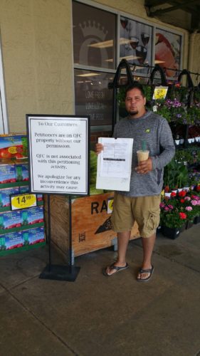 Petitioner next to a QFC sign about unsanctioned petitioning